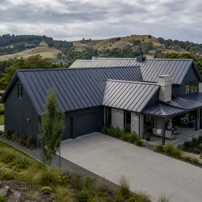 Modern farmhouse with a dark standing-seam steel roof against rolling hills