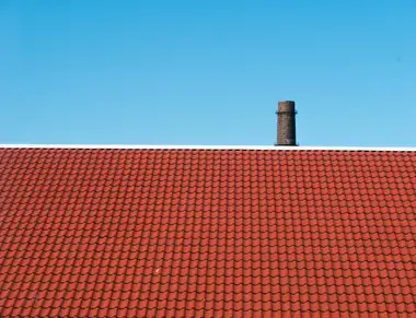 Freshly recoated tile roof and chimney under a clear blue sky