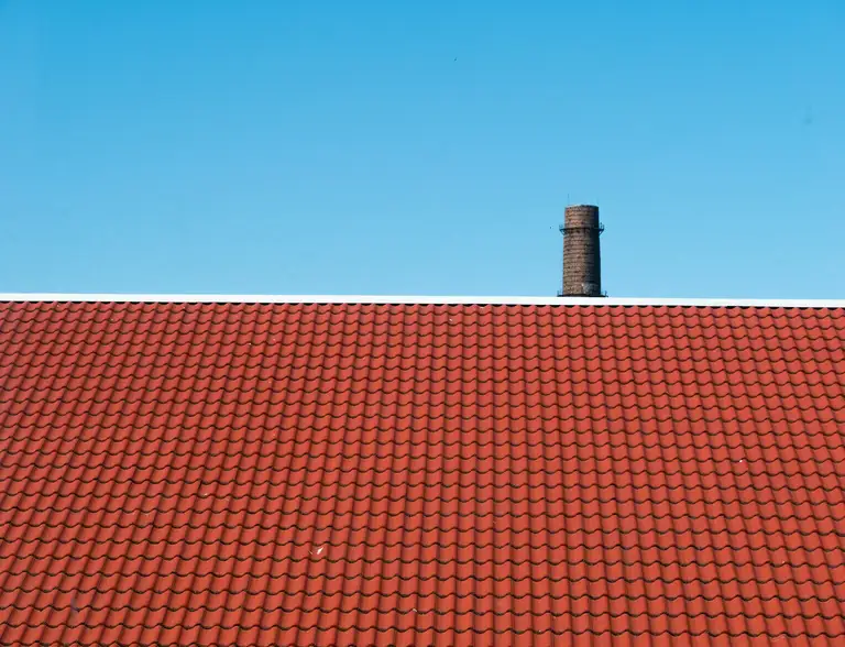 Freshly recoated tile roof and chimney under a clear blue sky
