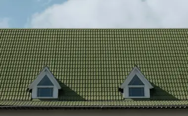 Pitched green tile roof with twin dormers against a clear blue sky