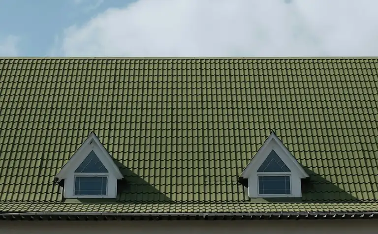 Pitched green tile roof with twin dormers against a clear blue sky